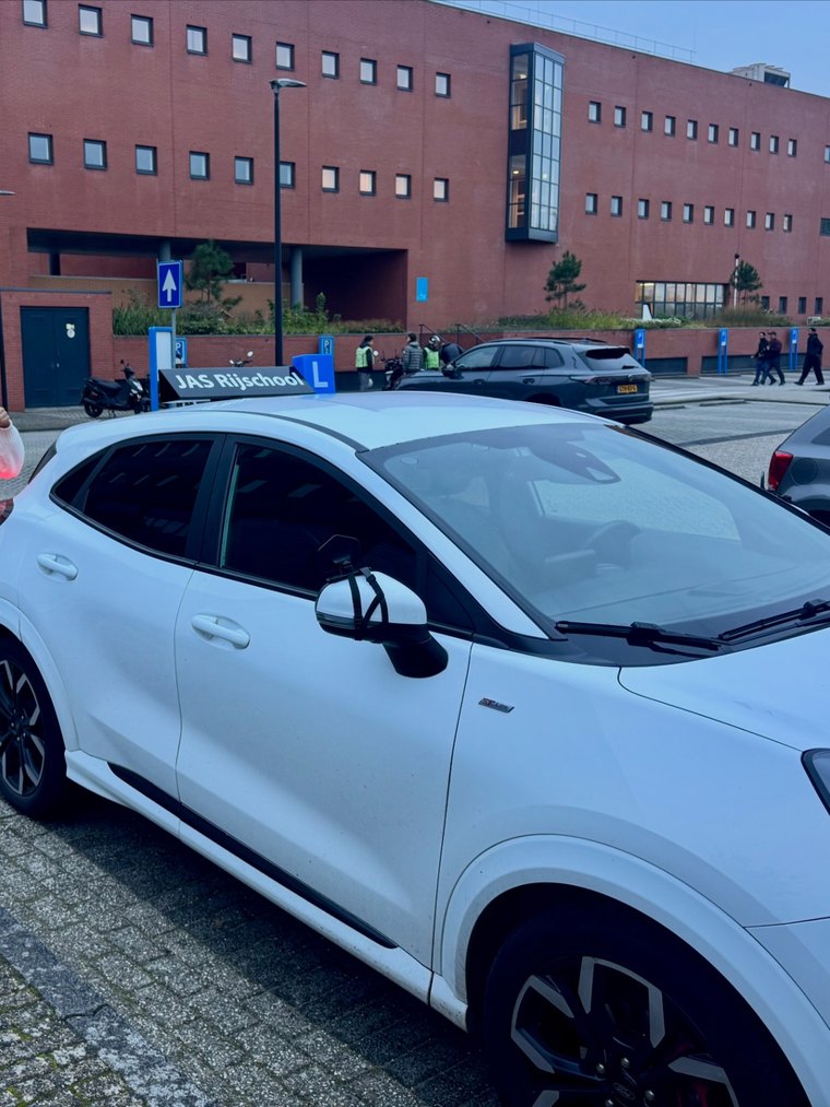 Geslaagde leerling met duim omhoog naast de lesauto van JAS-Rijschool
