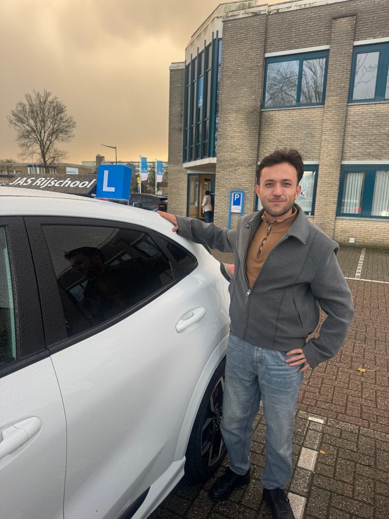 Geslaagde leerling naast de witte Ford Puma-lesauto van JAS-Rijschool