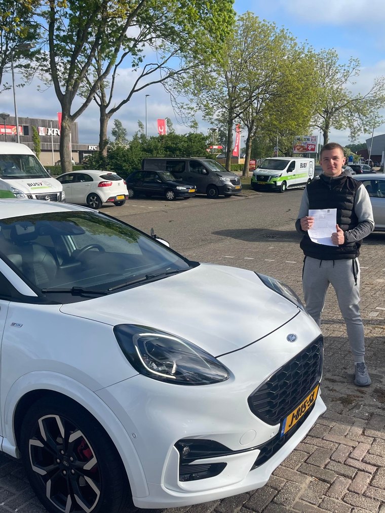 Geslaagde leerling met het examenformulier naast de lesauto van JAS-Rijschool